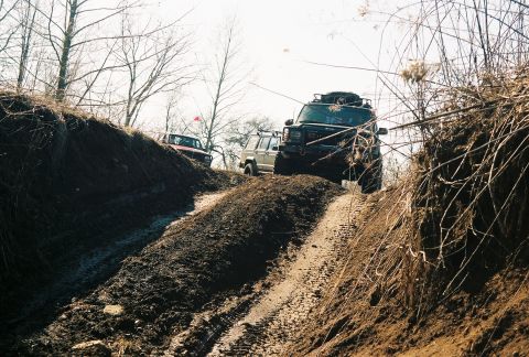 1995 Ford Bronco - Several SUVs are shown traversing a challenging off-road course with steep, muddy inclines.