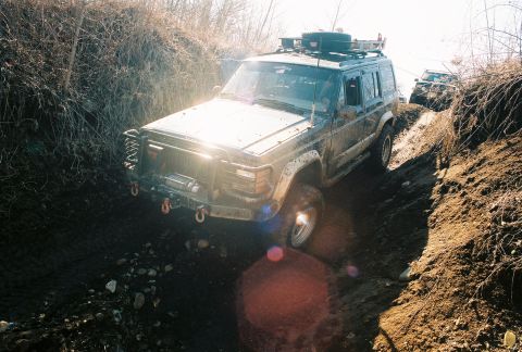 1995 Ford Bronco - A muddy Jeep Cherokee XJ navigates a steep, dirt path with another vehicle following behind.