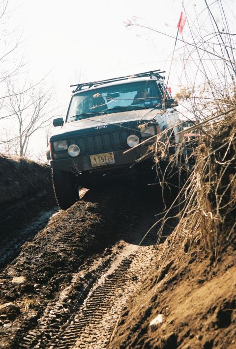 1995 Ford Bronco - Jeep Cherokee XJ navigates a challenging muddy incline during an off-road excursion.
