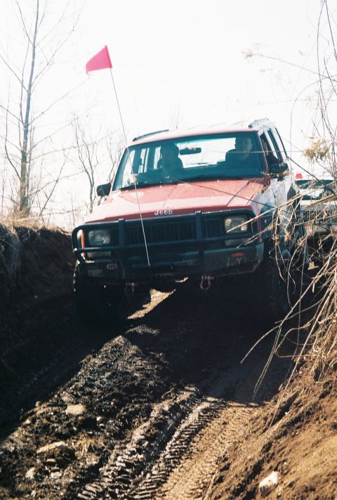 1995 Ford Bronco - Jeep Cherokee navigates a challenging muddy off-road course with a red flag on an antenna.
