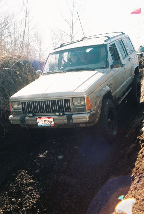 1995 Ford Bronco - This Jeep Cherokee XJ is navigating a challenging off-road trail with steep, muddy inclines.