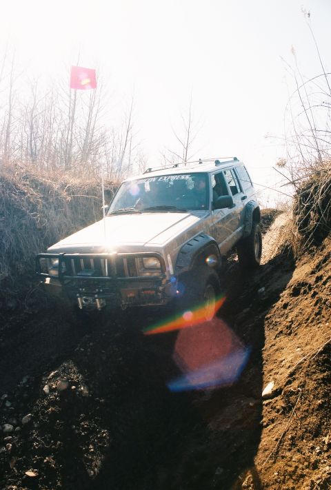 1995 Ford Bronco - A silver Jeep Cherokee XJ navigates a steep, muddy trail during an off-road excursion.
