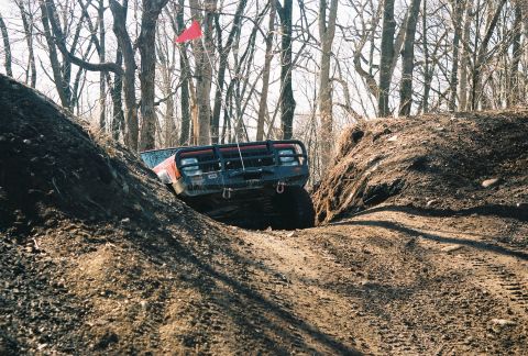 1995 Ford Bronco - An off-road vehicle navigates a challenging dirt track surrounded by trees.