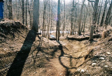 1995 Ford Bronco - A white SUV navigates a challenging dirt path through a wooded area.