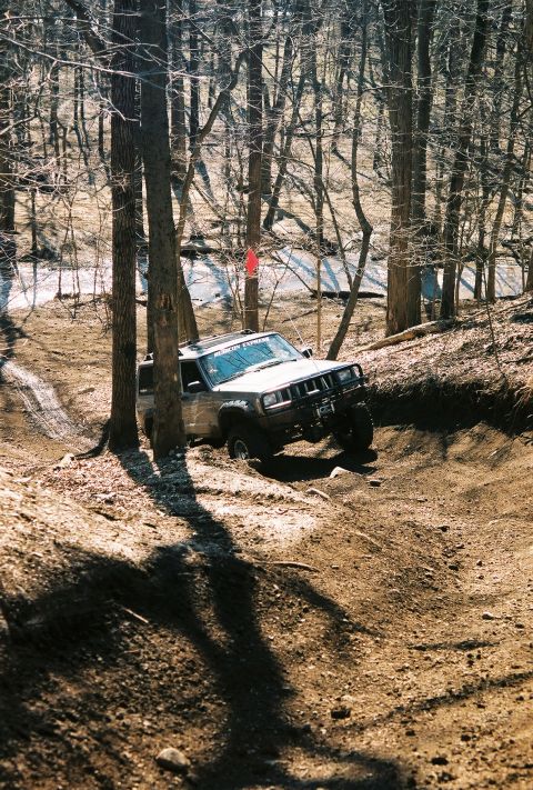 1995 Ford Bronco - A Jeep Cherokee XJ navigates a challenging off-road trail through a forest.