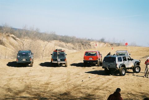 1995 Ford Bronco - Several SUVs are gathered on a sandy terrain under a clear sky.
