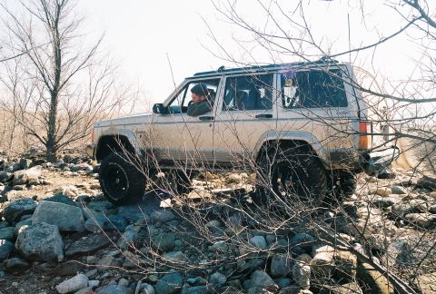 1995 Ford Bronco - A Jeep Cherokee XJ navigates a rocky, off-road terrain.