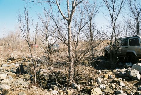 1995 Ford Bronco - Multiple SUVs traverse a challenging, rocky landscape under a clear sky.