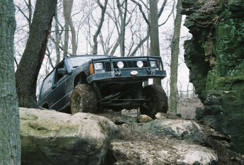 1995 Ford Bronco - A dark Jeep Cherokee XJ navigates a rocky, off-road trail during winter.