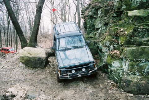 1995 Ford Bronco - Jeep Cherokee XJ tackles a challenging rocky off-road course with another vehicle in the distance.