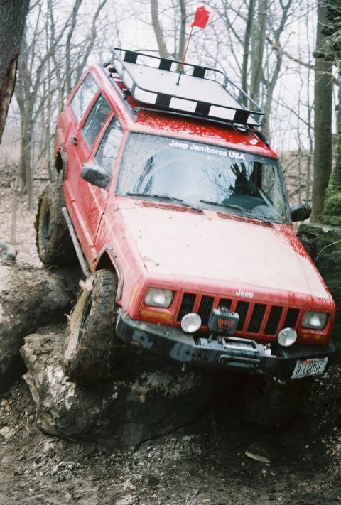 1995 Ford Bronco - This red Jeep Cherokee is shown tackling a challenging off-road course, demonstrating its capabilities.
