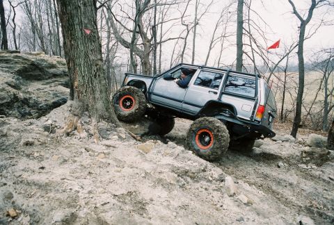 1995 Ford Bronco - A modified Jeep navigates a challenging off-road course with steep inclines and large rocks.