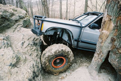 1995 Ford Bronco - A modified Jeep Cherokee Sport tackles a challenging off-road course with large tires and a roll cage.