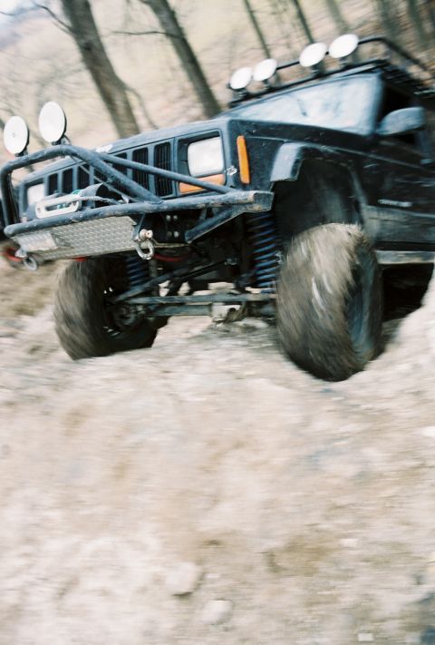 1995 Ford Bronco - Jeep Cherokee XJ navigates a rough dirt path, equipped for off-road adventures.