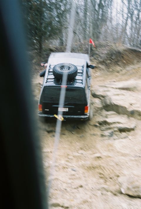 1995 Ford Bronco - An off-road SUV tackles a challenging dirt path, its spare tire secured on the roof rack.