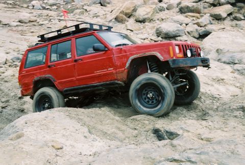 1995 Ford Bronco - A red Jeep Cherokee navigates a rocky off-road course, demonstrating its climbing capability.