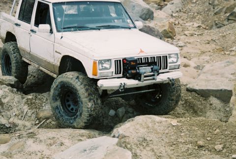 1995 Ford Bronco - A modified white Jeep Cherokee XJ navigates a challenging rocky obstacle course.