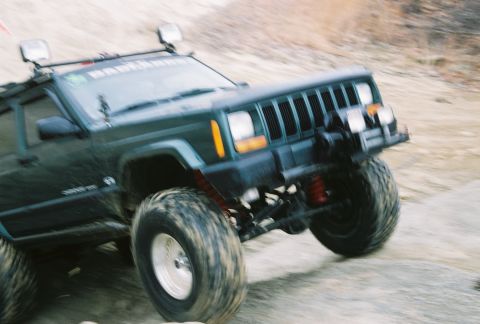 1995 Ford Bronco - A modified Jeep Cherokee XJ tackles a challenging off-road course, its suspension and tires clearly visible.