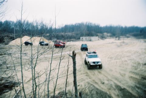 1995 Ford Bronco - A group of off-road vehicles navigates a sandy terrain under an overcast sky.