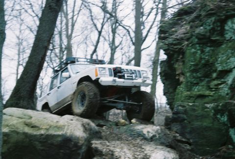 1995 Ford Bronco - An off-road SUV navigates a rocky trail in a wooded area.