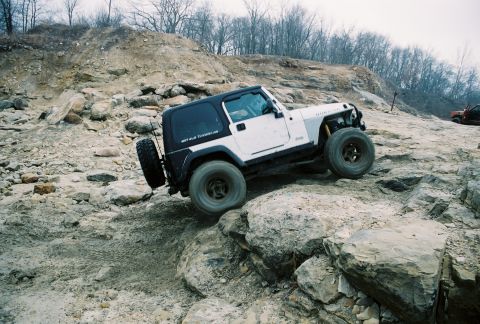 1995 Ford Bronco - A white Jeep Wrangler TJ navigates a rocky off-road course, with another vehicle visible in the background.