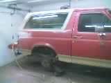 1989 Ford Bronco - Small, low-resolution shot of a red two-door SUV with a white removable hardtop sitting in a garage bay, viewed from the front three-quarte…