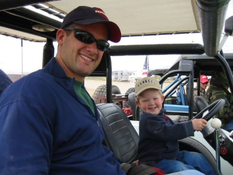 1992 Ford Bronco - A man and a child smile while sitting in a golf cart, with other vehicles visible in the distance.