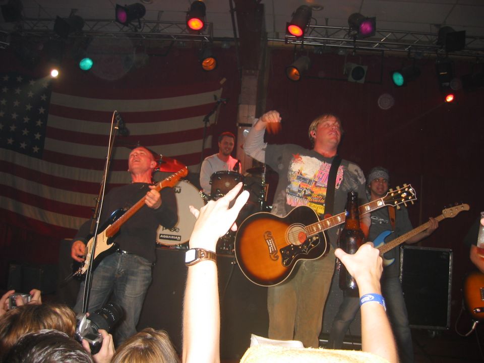 Band playing guitars and drums on stage in front of an American flag