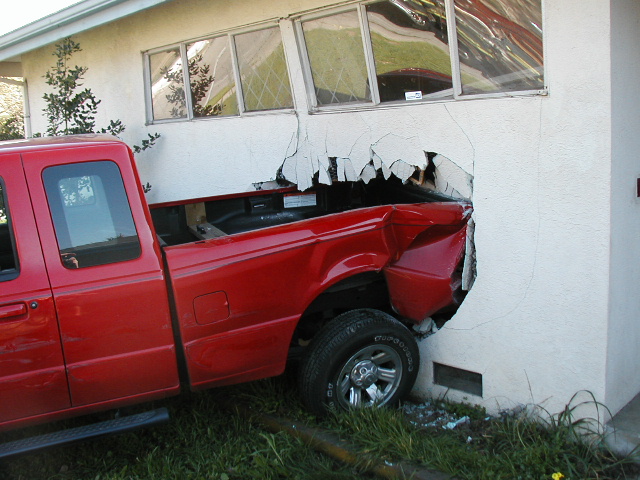 Red pickup truck rear-ended into a building wall, causing significant damage