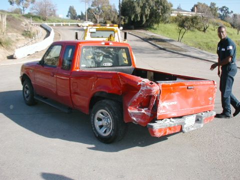 2000 Ford Ranger - A red pickup truck sustained heavy damage to its rear end, with a tow truck visible in the background.