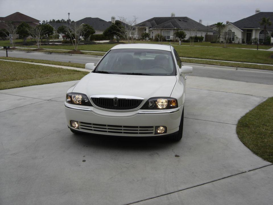 White Lincoln LS sedan front view with headlights on in a suburban driveway