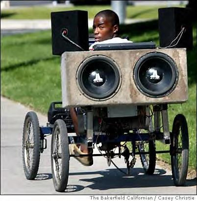 1990 Ford Bronco - A custom-built vehicle, a large speaker system, is seen from the side as it is driven by a young person.