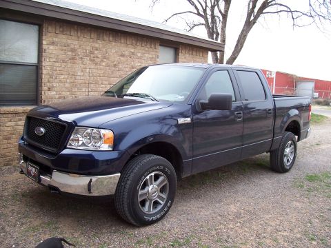 2005 Ford F-150 - A dark blue Ford F-150 pickup truck is parked on a gravel surface in front of a brick building.
