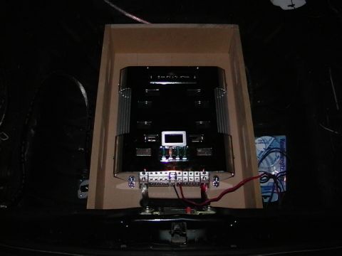 1995 Ford Contour - Dimly lit car-audio amplifier rack mounted in a trunk, with a black finned amplifier recessed in an angled MDF enclosure and a lit blue dis…