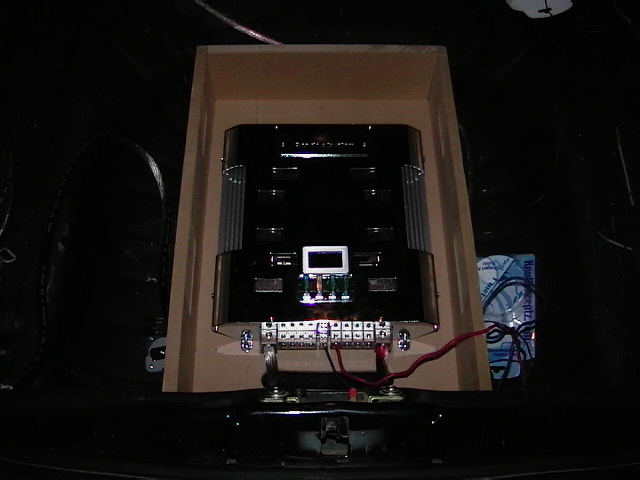 Trunk-mounted car audio amplifier in an angled MDF rack with red power wiring
