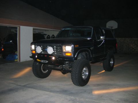 1985 Ford Bronco - Modified black Ford Bronco with large tires and auxiliary lighting parked in a driveway at night.