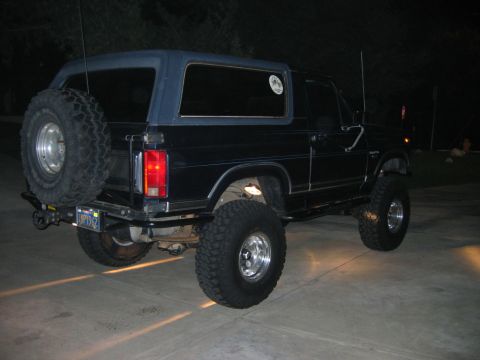 1985 Ford Bronco - This Ford Bronco has a dark blue soft top and is parked on a concrete surface at night.
