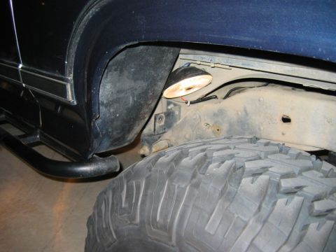 1985 Ford Bronco - A rock light is installed inside the wheel well of a dark blue SUV, near the tire.