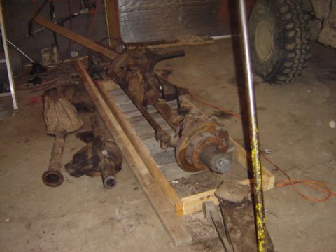 1992 Ford Bronco - Two heavily rusted axle assemblies are laid out on wooden planks inside a garage.