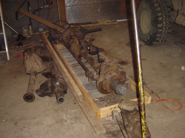 Rusty axle assemblies on wooden pallets in a garage, with a large tire visible in the background