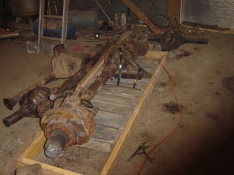 1992 Ford Bronco - Multiple vehicle axles are stored on a wooden pallet in a workshop setting.