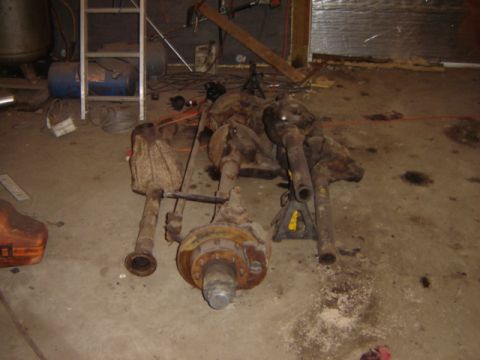 1992 Ford Bronco - Multiple vehicle axle assemblies and differential parts are piled on a garage floor.