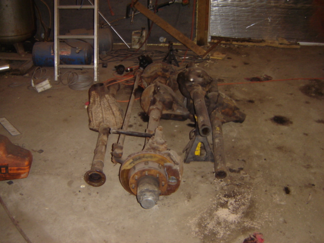 Several rusty vehicle axles and differential assemblies on a concrete floor