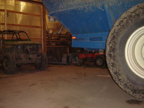 1992 Ford Bronco - A green off-road vehicle is parked inside a garage next to a large blue trailer and other equipment.