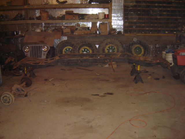 Jeep CJ-6 chassis and front clip with grille and headlights, supported by jack stands in a garage