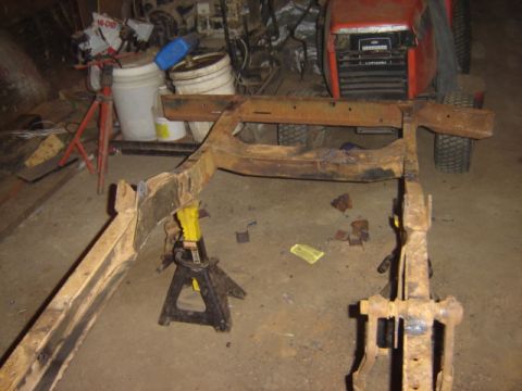 1992 Ford Bronco - A heavily rusted vehicle frame is supported by jack stands in a cluttered garage setting.
