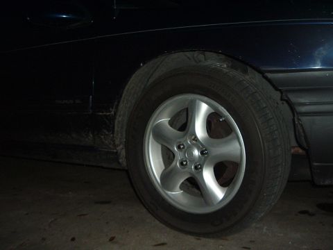 1993 Ford Taurus - A dark blue 1993 Ford Taurus DL is shown from the side, focusing on the front wheel and fender area.