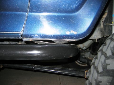 1985 Ford Bronco - This image shows the side panel and undercarriage of a blue SUV, with a black step and a large tire in view.
