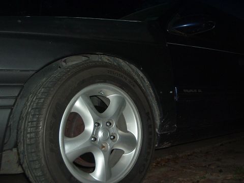 1993 Ford Taurus - A dark sedan, identified as a 1993 Ford Taurus GL, is viewed from the side, focusing on the front wheel and door panel.