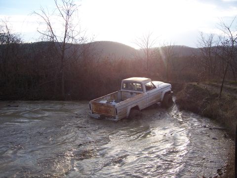 1999 Jeep TJ - A white pickup truck navigates through a muddy off-road trail, its tires submerged in the muck.